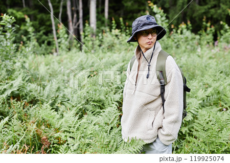 Vibrant shot of Asian man as male tourist standing in green fern undergrowth while exploring forest alone and looking away copy space 119925074