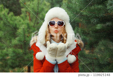Happy young woman in winter park against Christmas tree, girl in white hat, glasses in snowy forest 119925148