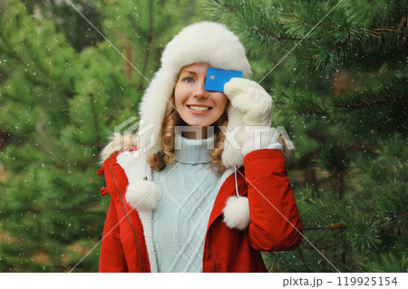 Happy smiling young woman holding plastic credit bank card in winter park against Christmas tree Happy smiling young woman holding plastic credit bank card in winter park against Christmas tree 119925154