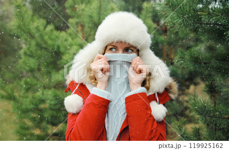 Woman is cold, freezing trying to warm up outdoors in winter park against Christmas tree in forest 119925162