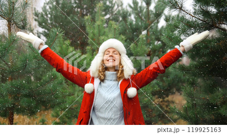 Winter day, happy smiling young woman enjoys snow, warm weather against Christmas tree Winter day, happy smiling young woman enjoys snow, warm weather against Christmas tree 119925163