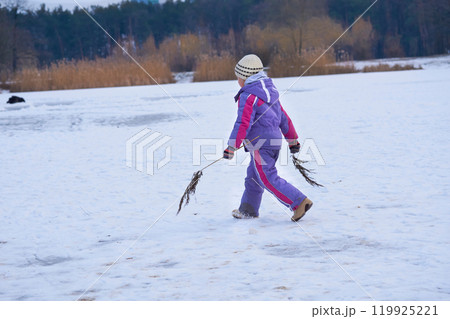 Playful child girl walks on a frozen lake in a winter forest park Playful child girl walks on a frozen lake in a winter forest park 119925221