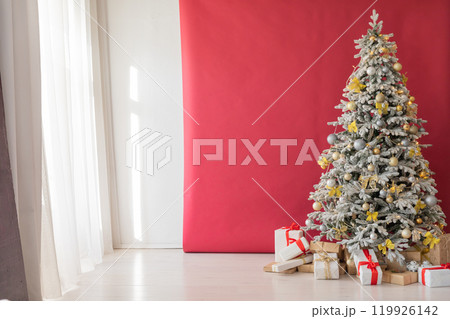 Christmas tree with gifts decorated with toys in the interior of a red and white room for the new year Christmas tree with gifts decorated with toys in the interior of a red and white room for the new year 119926142