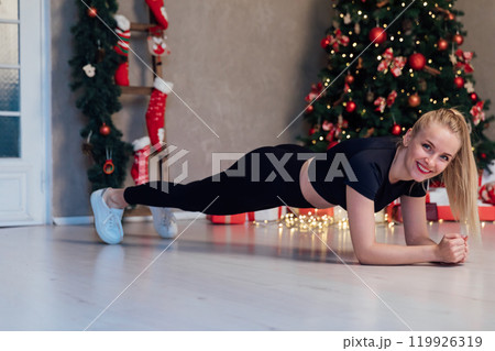 Beautiful blonde woman doing fitness push-ups sports gymnastics at the christmas tree for new year Beautiful blonde woman doing fitness push-ups sports gymnastics at the christmas tree for new year 119926319