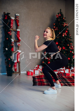 blonde woman doing fitness sport gymnastics at christmas tree for new year blonde woman doing fitness sport gymnastics at christmas tree for new year 119926320
