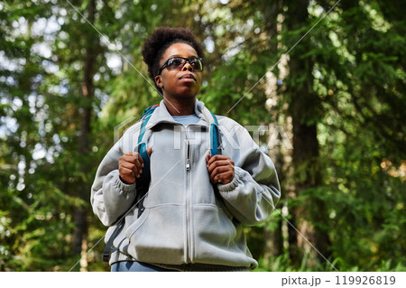 Low angle portrait of active Black young woman hiking solo in green forest, copy space 119926819