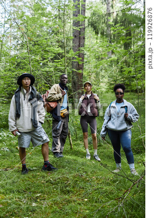 Multiethnic group of tourists standing outdoors on forest path and looking at camera while hiking together 119926876