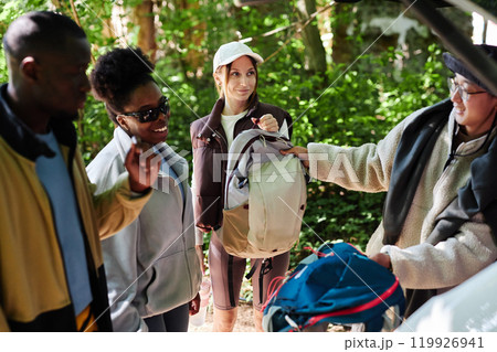 Multiethnic group of people as tourists unloading hiking gear from car trunk ready to explore green forest together 119926941