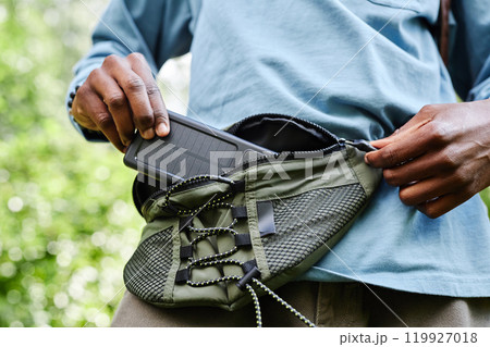 Close up of male hands holding power bank with solar battery and taking out of belt bag while hiking in forest copy space 119927018