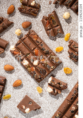 Broken chocolate pieces with nuts and raisins on a stone background top view Broken chocolate pieces with nuts and raisins on a stone background top view 119928104