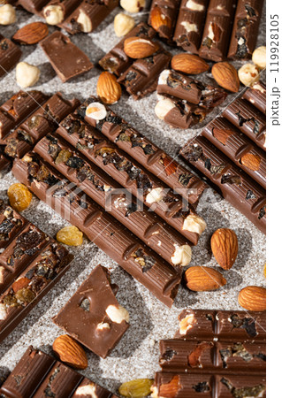 Broken chocolate pieces with nuts and raisins on a stone background top view Broken chocolate pieces with nuts and raisins on a stone background top view 119928105