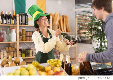 Female vendor in Irish green cap offers Irish ale to male customer 119928318