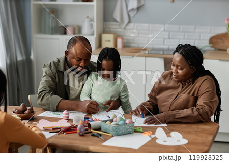 Family enjoying quality time together sitting at table doing arts and crafts activity Parents and children collaborating and creating colorful art pieces 119928325
