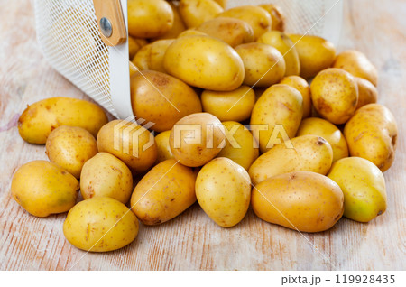 Raw potatoes in white wire basket on wooden background Raw potatoes in white wire basket on wooden background 119928435