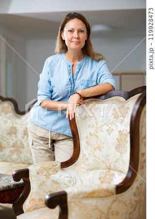 Calm female standing and leaning on the chair in the living room at home Calm female standing and leaning on the chair in the living room at home 119928473