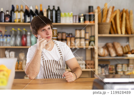 Portrait of confident young salesperson sitting at counter in supermarket 119928489