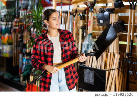 Young female gardener choosing shovel at garden market 119928520