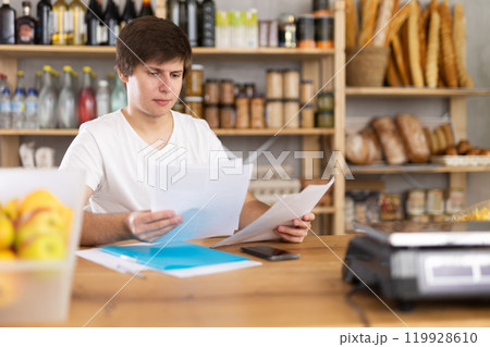 Young male seller examines documents in grocery store Young male seller examines documents in grocery store 119928610
