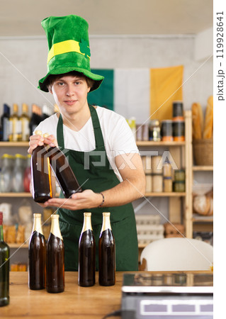 Positive male store clerk in green hat is preparing to meet customers on eve of St. Patricks Day. 119928641
