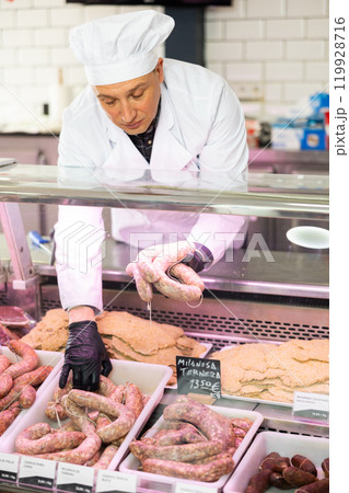 Butcher arranging raw sausages on display with price tags on Spanish 119928716