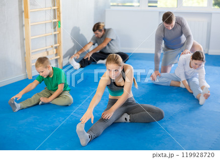 Family in gym during group sports training under guidance of trainer performs stretching on floor 119928720