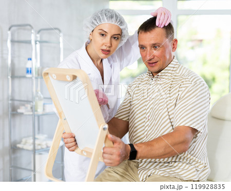 Portrait of man sitting on couch and looking at mirror during appointment with doctor at clinic Portrait of man sitting on couch and looking at mirror during appointment with doctor at clinic 119928835