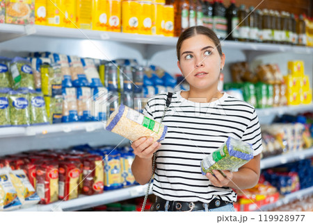 Thinking girl stands in supermarket and chooses pack of cereals 119928977