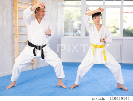 Individual karate lesson for teenager - fighting position of teenager and coach during karate training in gym Individual karate lesson for teenager - fighting position of teenager and coach during karate training in gym 119929143