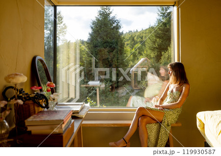 Woman Reflecting by the Window with a Scenic Garden View 119930587