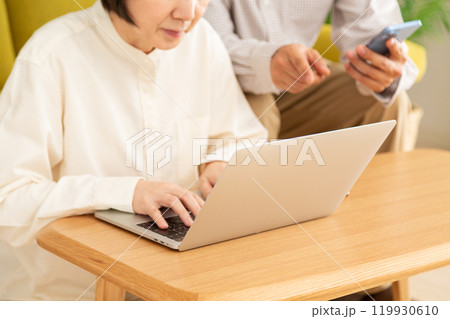 リビングでパソコンとスマホを見るミドル〜シニア夫婦 リビングでパソコンとスマホを見るミドル〜シニア夫婦 119930610