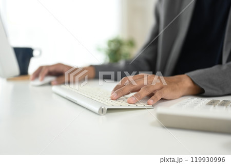 Close up of businessman typing on wireless keyboard at modern workspace Close up of businessman typing on wireless keyboard at modern workspace 119930996