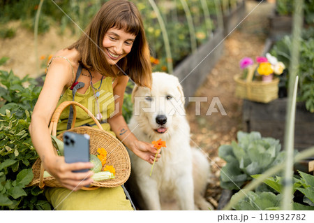 Woman in a green apron takes a selfie with her dog in her eco-friendly garden Woman in a green apron takes a selfie with her dog in her eco-friendly garden 119932782