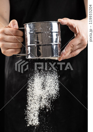 The cook sifts the wheat flour through a metal sieve. 119933204