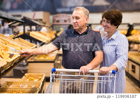 Mature family of retirees examines bread and pastries in grocery section of a supermarket 119936187