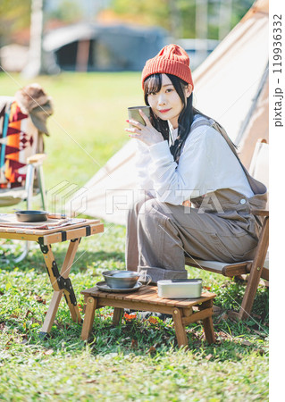 キャンプで飲み物を飲みリラックスするニット帽をかぶった若い女性 119936332
