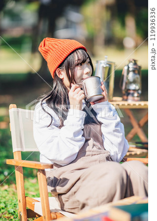 キャンプで飲み物を飲みリラックスするニット帽をかぶった若い女性 119936336