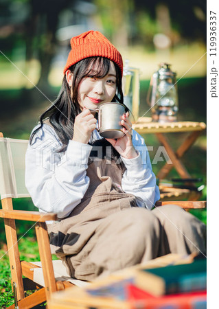 キャンプで飲み物を飲みリラックスするニット帽をかぶった若い女性 119936337