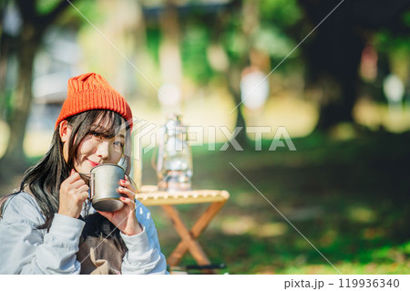 キャンプで飲み物を飲みリラックスするニット帽をかぶった若い女性 キャンプで飲み物を飲みリラックスするニット帽をかぶった若い女性 119936340