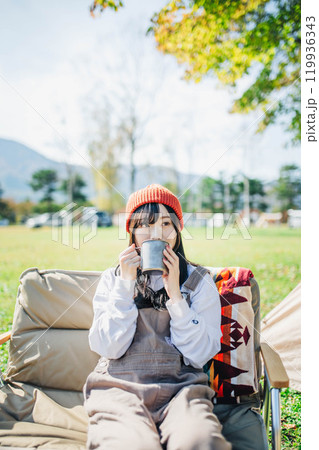 キャンプで飲み物を飲みリラックスするニット帽をかぶった若い女性 キャンプで飲み物を飲みリラックスするニット帽をかぶった若い女性 119936343