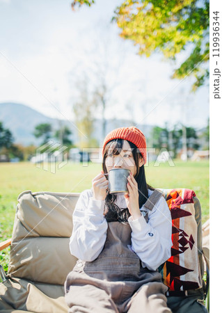 キャンプで飲み物を飲みリラックスするニット帽をかぶった若い女性 キャンプで飲み物を飲みリラックスするニット帽をかぶった若い女性 119936344