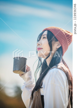 キャンプで飲み物を飲みリラックスするニット帽をかぶった若い女性 キャンプで飲み物を飲みリラックスするニット帽をかぶった若い女性 119936346