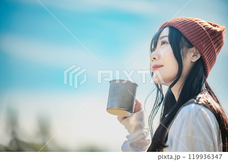 キャンプで飲み物を飲みリラックスするニット帽をかぶった若い女性 119936347