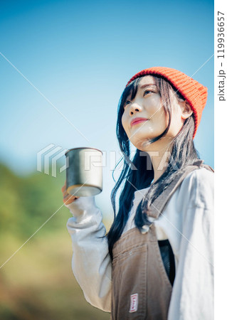 青空のもとで飲み物を飲むニット帽を被った若い女性 119936657
