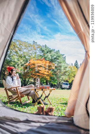 キャンプで飲み物を飲みながらリラックスする若い女性 119936809