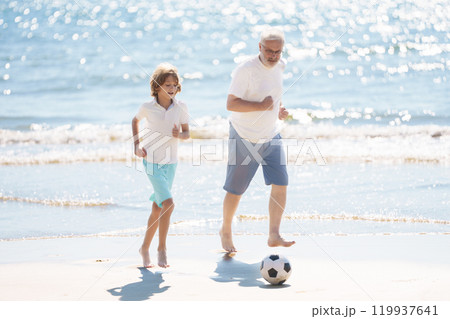 Grandfather and kids play football on beach. 119937641