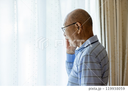 外を眺めながら電話をするシニア男性 119938059