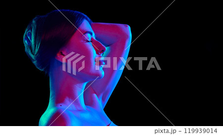 Side view of young serene woman with closed eye expressing relax and joy in bright neon light against black studio background. 119939014