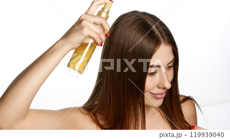 Young brunette woman spraying hair for healthy shine against white background. Haircare routine. Young brunette woman spraying hair for healthy shine against white background. Haircare routine. 119939040