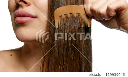 Close-up of a woman combing her hair, showcasing natural hair care against white background, with focus on texture. 119939046