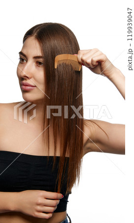 Woman brushing her hair with wooden comb, focusing on simple, natural hair care practices against white background. 119939047